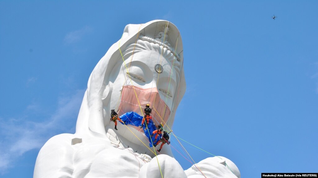 日本福島的工人給57米高的觀音菩薩雕像“帶”上口罩，祈禱新冠疫情早日結束。（路透社）
