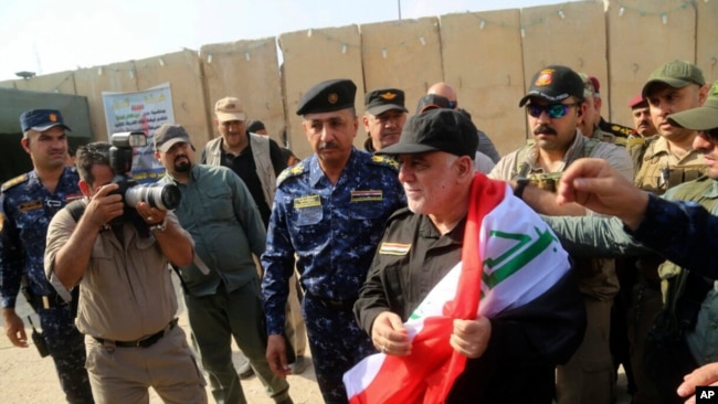 Iraq's Prime Minister Haider al-Abadi, center, holds a national flag upon his arrival to Mosul, Iraq, July 9, 2017.