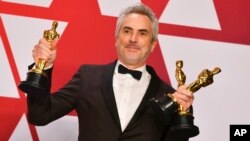 FILE - Alfonso Cuaron poses with the awards for best director for "Roma," best foreign language film for "Roma," and best cinematography for "Roma" in the press room at the Oscars at the Dolby Theatre in Los Angeles, Feb. 24, 2019.