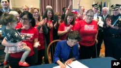 FILE - Cheers erupt as Rhode Island Gov. Gina Raimondo signs an executive order, Feb. 26, 2018, in Warwick, R.I., to establish a new policy to try to keep guns away from people who show warning signs of violence. 