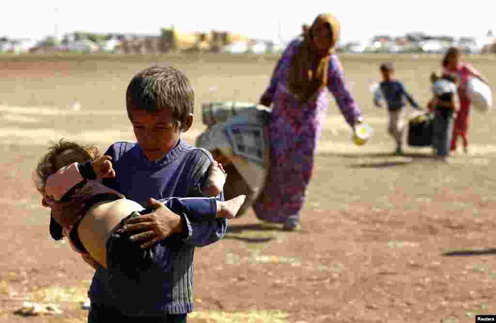 A young Syrian Kurdish refugee boy carries a young child after crossing the Syrian-Turkish border, near the southeastern town of Suruc in Sanliurfa province. 