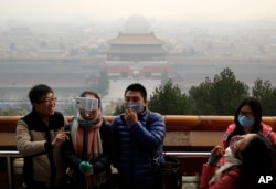 Visitors, some wearing masks to protect themselves from pollutants, take a selfie Dec. 7, 2015, at the Jingshan Park in Beijing. Smog shrouded the capital city Monday after authorities in Beijing issued an orange alert Saturday.