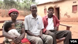 Silas Bihizi, center, sits with Valens Rukiriza, right, Rukiza's wife and one of their grandchildren outside the Rukiza family home in Buguli, Rwanda.