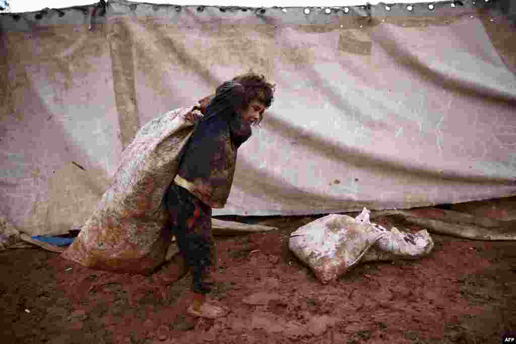 A Syrian child carries a sack in the mud at a camp for the displaced near the village of Shamarin, near the border with Turkey in the northern Aleppo province.