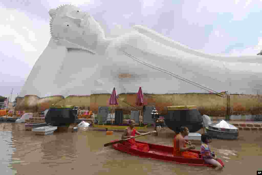 Buddhist monks paddle a boat through floodwaters in front of a reclining Buddha at the Wat Satue in Ayutthaya province north of Bangkok.