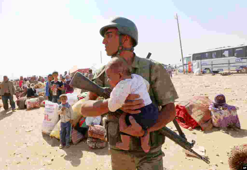A Turkish soldier holds a lost baby as he looks for its mother, as thousands of new Syrian refugees from Kobani arrive at the Turkey-Syria border crossing of Yumurtalik near Suruc, Turkey, Oct. 2, 2014. 