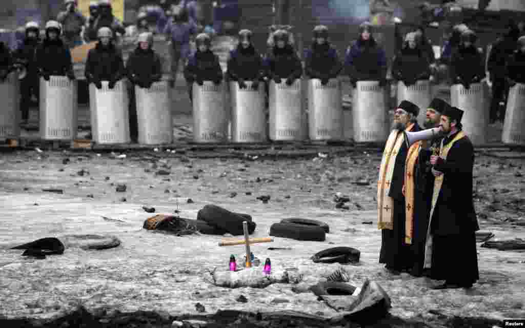 A priest speaks through a megaphone to riot police and anti-government protesters at the site of recent clashes in Kyiv, Ukraine.