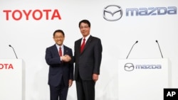 FILE - Toyota Motor Corp. President Akio Toyoda, left, and Mazda Motor Corp. President Masamichi Kogai pose for photographers before a press conference in Tokyo, May, 13, 2015. The Japanese automakers are partnering in electric vehicles with a deal expected to be announced Friday.