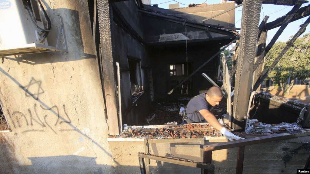 An Israeli police officer inspects a house badly damaged by a suspected attack by Jewish extremists in the West Bank village of Duma July 31, 2015. The Hebrew text on house's wall reads "revenge."