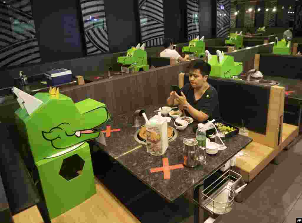 A customer uses a mobile phone while sitting with a cartoon dragon dolls the restaurant uses as space keepers for social distancing to help curb the spread of the coronavirus at shopping mall in Bangkok, Thailand, Monday, May 18, 2020. (AP Photo/Sakchai 