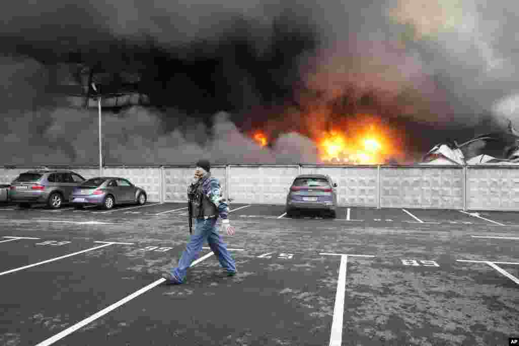 A Ukrainian serviceman walks past as fire and smoke rises over a damaged logistic center after shelling in Kyiv, Ukraine, March 3, 2022. 