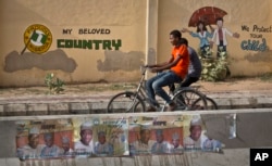 Two youths ride bicycles past a mural on a school wall and election posters supporting President Goodluck Jonathan, on a street in Kano, Nigeria Sunday, March 29, 2015.