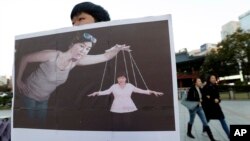 FILE - A South Korean college student holds a placard depicting South Korea's President Park Geun-hye (right bottom) as a marionette and Choi Soon-sil, who is at the center of a political scandal, as a puppeteer, in Seoul, South Korea, Nov. 3, 2016. 