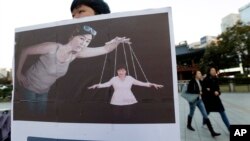 A South Korean college student holds a placard depicting South Korea's President Park Geun-hye, right bottom, as a marionette and Choi Soon-sil, who is at the center of a political scandal, as a puppeteer, in Seoul, South Korea, Nov. 3, 2016. 