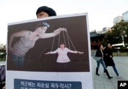 FILE - A South Korean college student holds a placard depicting South Korea's President Park Geun-hye, right bottom, as a marionette and Choi Soon-sil, who is at the center of a political scandal, as a puppeteer, in Seoul, South Korea, Nov. 3, 2016.