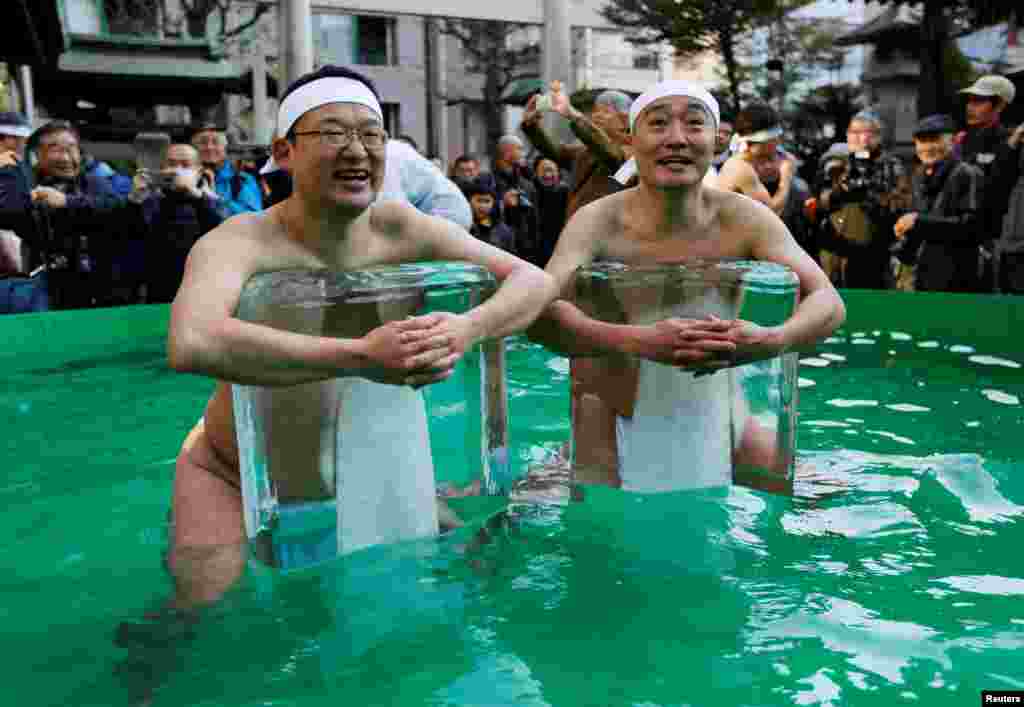 Dua pria yang hanya mengenakan kain di pinggang, menahan bongkahan es batu di kolam air dingin selama upacara untuk memurnikan jiwa dan berharap kesehatan yang baik di kuil Teppozu Inari, Tokyo, Jepang.