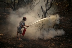 A woman uses a fire extinguisher to save a burning tree in Cokertme village, near Bodrum, Mugla, Turkey, Tuesday, Aug. 3, 2021. (AP Photo/Emre Tazegul)