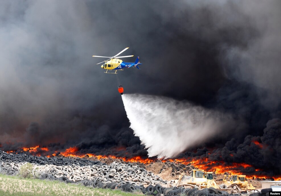 An helicopter throws water over a fire at a tire dump near a residential development in Sesena, south of Madrid, Spain.