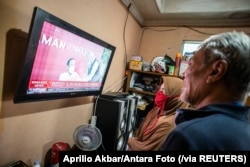 Warga menyaksikan siaran langsung Presiden Joko Widodo disuntik perdana vaksin Covid-19 di Jakarta, Rabu, 13 Januari 2021. (Foto: Aprilio Akbar/Antara Foto via Reuters)