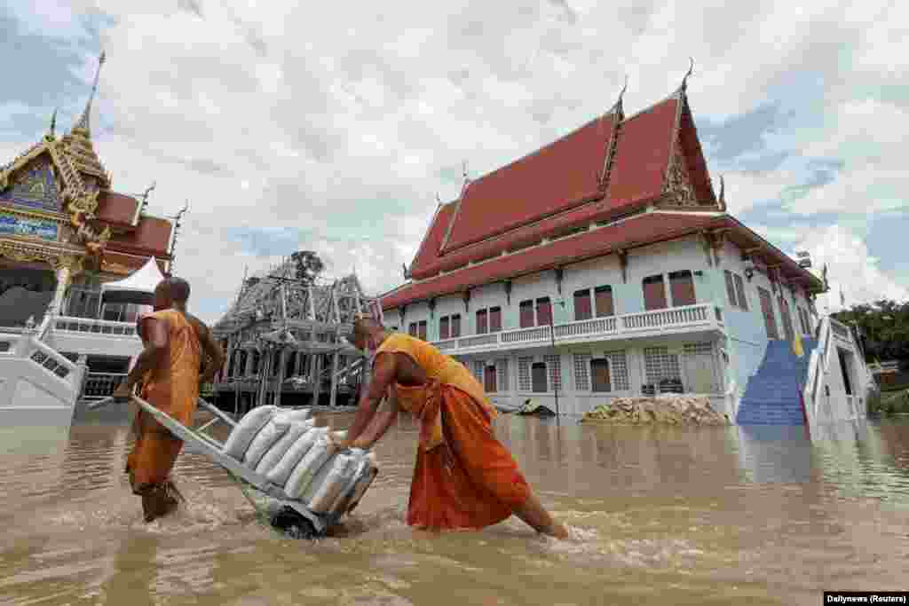 Dua biksu Buddha menarik kereta yang mengangkut karung-karung pasir untuk melindungi kuil mereka dari banjir di provinsi Ayutthaya, Thailand (Foto: Dailynews via Reuters).