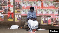 A woman sits in front of campaign posters as she waits to cast her ballot, during the Jubilee Party primary elections, at a polling centre in Nairobi, Kenya.