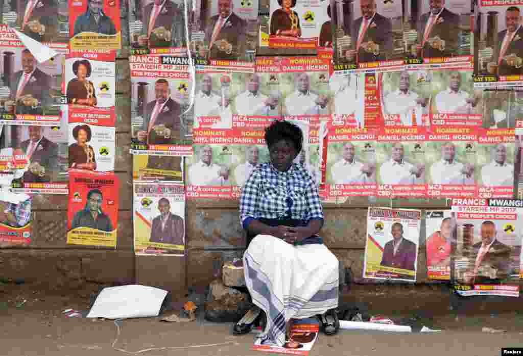 A woman sits in front of campaign posters as she waits to cast her ballot, during the Jubilee Party primary elections, at a polling centre in Nairobi, Kenya.