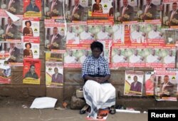 FILE - A woman sits in front of campaign posters as she waits to cast her ballot at a polling center in Nairobi, Kenya.