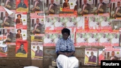 FILE - A woman sits in front of campaign posters as she waits to cast her ballot, during the Jubilee Party primary elections, at a polling centre in Nairobi, Kenya.