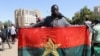 FILE - A man holds his national flag to show support for the military after Burkina Faso President Roch Kabore was detained at a military camp in Ouagadougou, Burkina Faso, Jan. 24, 2022.