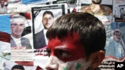 An anti-government protester, with his face painted in the colors of Yemen's and Syria's national flags, walks past pictures of people killed in anti-government clashes, during a rally demanding the ouster of Yemeni President Ali Abdullah Saleh, in Sanaa,