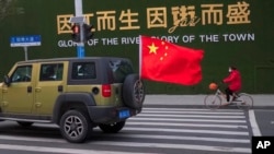 中國武漢街頭一輛插著中國國旗的汽車從一名戴著口罩騎車的婦女身邊駛過。 （2020年1月29日）