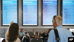 FILE - Passengers check arrival and departure displays at O'Hare International Airport in Chicago, Illinois, Sept. 27, 2014.