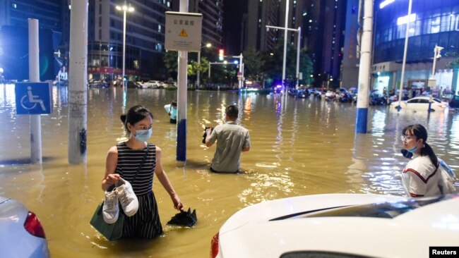 中国安徽合肥的民众在被洪水淹没的街道上过马路。（2020年6月27日）