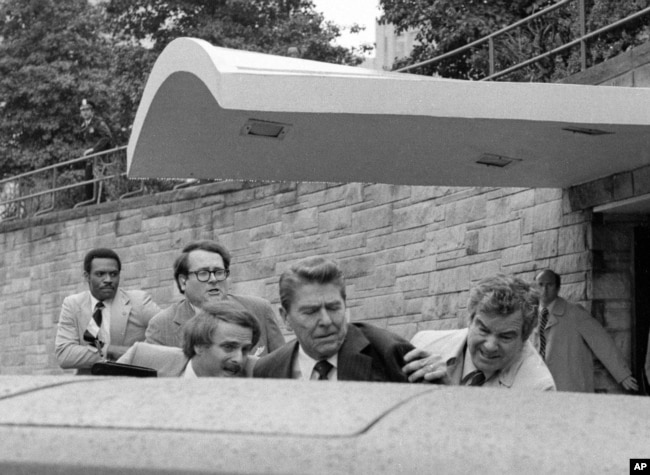 FILE - U.S. President Ronald Reagan waves and then looks up before being shoved into the President's limousine by secret service agents after being shot outside a Washington hotel Monday, March 30, 1981. (AP Photo/Ron Edmonds)