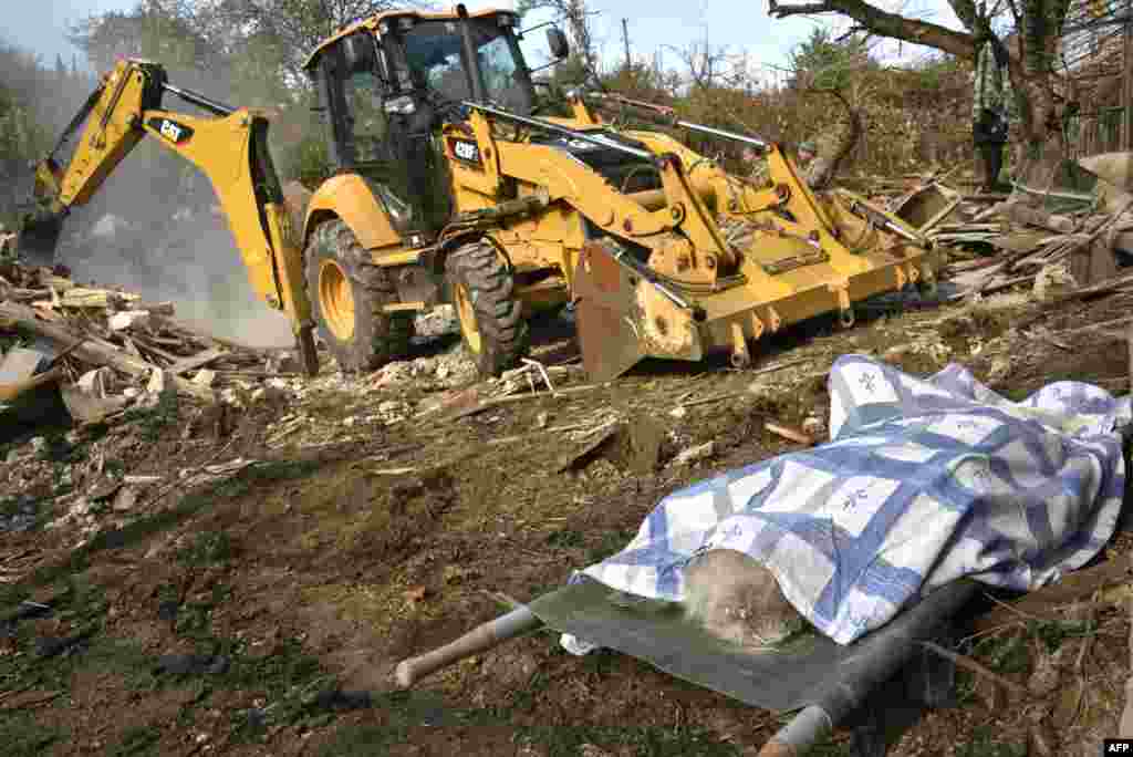 The body of a woman lays on a stretcher near a bulldozer clearing debris of a destroyed house hit by shelling during the military conflict between Armenia and Azerbaijan over Nagorno-Karabakh, in the disputed province&#39;s capital of Stepanakert.
