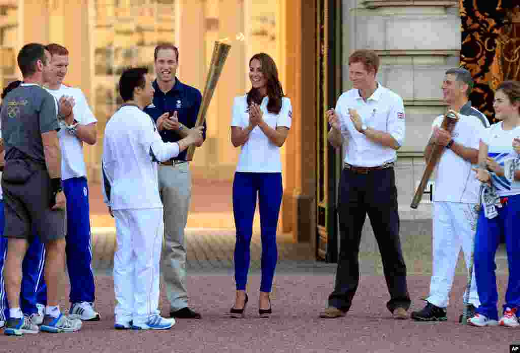 This photo provided by LOCOG shows torchbearer 170 passing the Olympic Flame to Torchbearer 171 in front of Buckingham Palace in the presence of the Duke and Duchess of Cambridge and Prince Harry, July 26, 2012. 