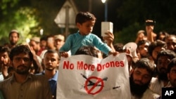 FILE - A boy holds a banner while sitting on his father's shoulder attending a rally called by the Pakistan Defense Council, a coalition of Islamic parties, in Lahore, Pakistan, June 12, 2016. Hundreds of supporters of the coalition rallied in Lahore against U.S. drone strikes in Pakistani areas.