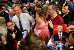 A man holds a photograph of Republican presidential candidate Jeb Bush as Bush greets people after a campaign event in Salem, N.H., Feb. 7, 2016.