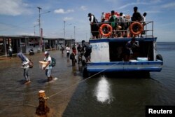 FILE - Passengers of a boat walk through rising sea water during high tide at Kali Adem port in Jakarta, Indonesia, Jan. 4, 2018.