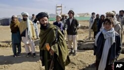 FILE - An Afghan plaincloth security personnel, holds his weapon as he walks among Pakistani refugees, at Gulan camp, some 20 kilometers (12 miles) from the border in the restive Khost province, Afghanistan, Jan. 19, 2015.