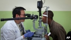 FILE - Dr. Zan Yeong, an eye specialist for the Partnership for Research on Ebola Vaccine in Liberia, examines the eyes of Ebola survivor Abraham Moses, who has problems with his vision, at the John F. Kennedy Medical Center in Monrovia, Liberia, July 31, 2015.