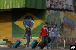 In this March 9, 2018 photo, young Venezuelans pull their luggage after crossing the border to Pacaraima, Roraima state, Brazil.