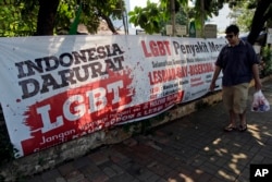 A man walks past an anti-LGBT banner with writings that read "Indonesia is on LGBT emergency" and "LGBT is a contagious disease, save the young generation from LGBT people."