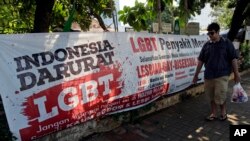 FILE - A man walks past an anti-LGBT banner with writings that read "Indonesia is on LGBT emergency" and "LGBT is a contagious disease, save the young generation from LGBT people," outside the headquarters of a conservative Islamic group in Jakarta, Indonesia, March 17, 2016.