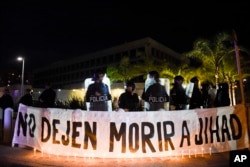 FILE - A sign that reads in Spanish "Don't let Jihad die" hangs behind candles outside the U.S. embassy during a demonstration in Montevideo, Uruguay, Sept. 16, 2016. Former Guantanamo detainee Abu Wa'el Dhiab from Syria, also called Jihad, was on a hunger strike, threatening to die if he was not allowed to reunite with his family elsewhere, after he was resettled in Uruguay.