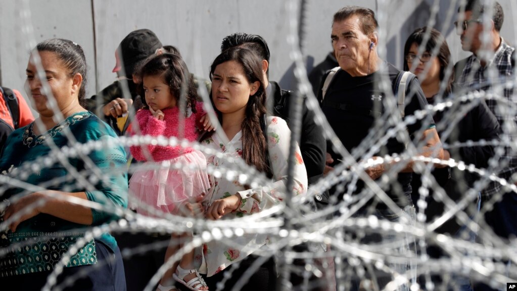 Los migrantes hacen fila para cruzar a EE.UU. desde Tijuana, México, a través de barreras de alambre de púa en San Diego, el 19 de noviembre de 2018.
