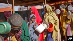 FILE - Newly-arrived women who fled drought queue to receive food distributed by local volunteers at a camp for displaced persons in the Daynile neighborhood on the outskirts of the capital Mogadishu, in Somalia, May 18, 2019.