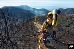 In this photo provided by the Santa Barbara County Fire Department, Santa Barbara County Firefighters haul dozens of pounds of hose and equipment down steep terrain below E. Camino Cielo to root out and extinguish smoldering hot spots in Santa Barbara, Calif., Dec. 19, 2017.