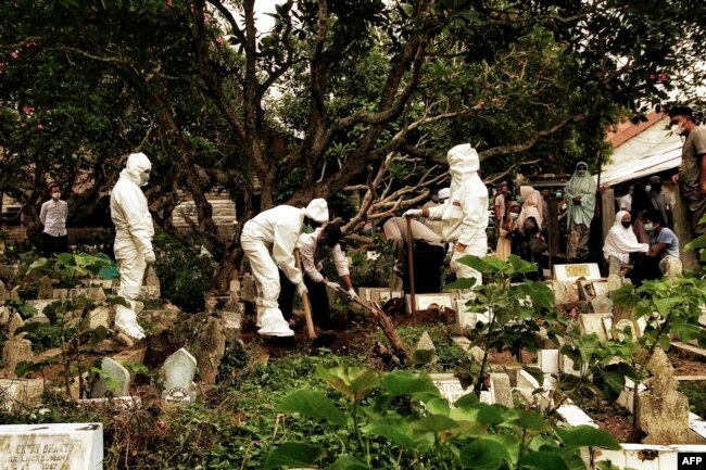 Penggali kuburan mengenakan pakaian pelindung diri (APD) mengubur korban COVID-19 di pemakaman di Lhokseumawe, Aceh, 18 Mei 2021. (Foto: Azwar Ipank / AFP)