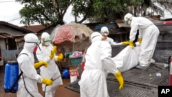 Health workers carry load the body of a woman that they suspect died from the Ebola virus, onto a truck in front of a makeshift shop in an area known as Clara Town in Monrovia, Liberia, Wednesday, Sept. 10, 2014.